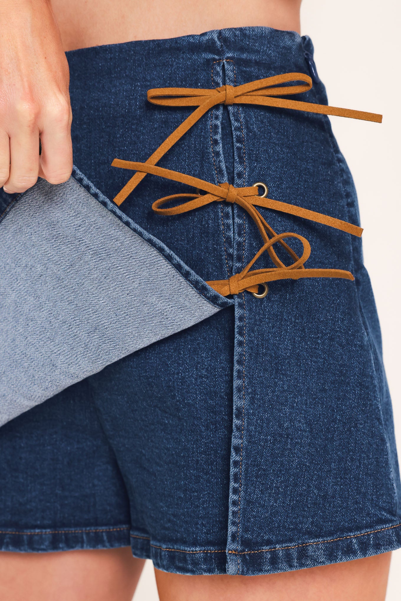 A woman wearing a blue denim mini skort featuring lace-up details on the side | Flying Tomato