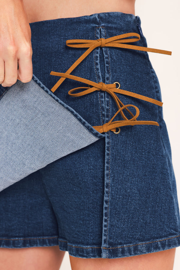 A woman wearing a blue denim mini skort featuring lace-up details on the side | Flying Tomato