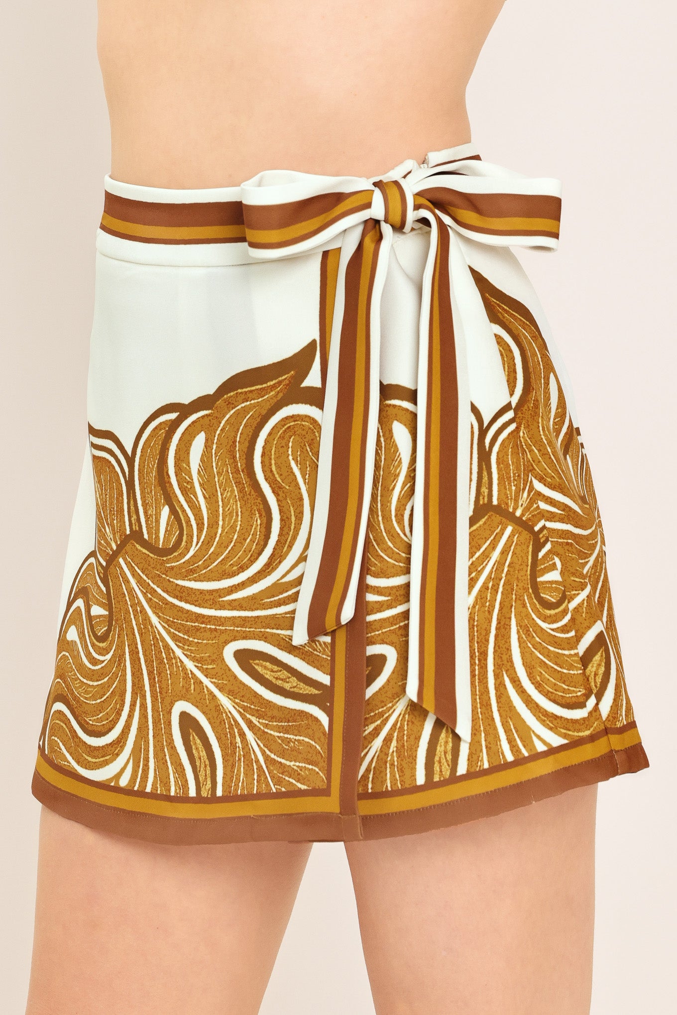 Woman wearing an ivory with brown leaf like print skort with a waist tie | Flying Tomato