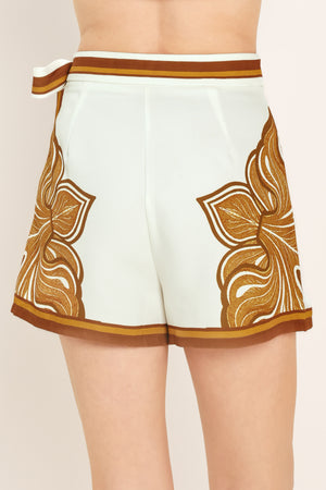Woman wearing an ivory with brown leaf like print skort with a waist tie | Flying Tomato
