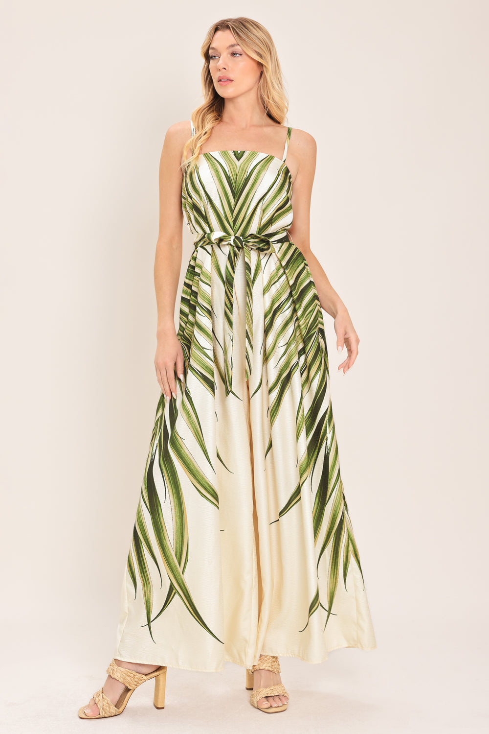 Woman wearing a green and beige wide-leg leaf-patterned jumpsuit featuring straight neckline, straps, and self tie | Flying Tomato