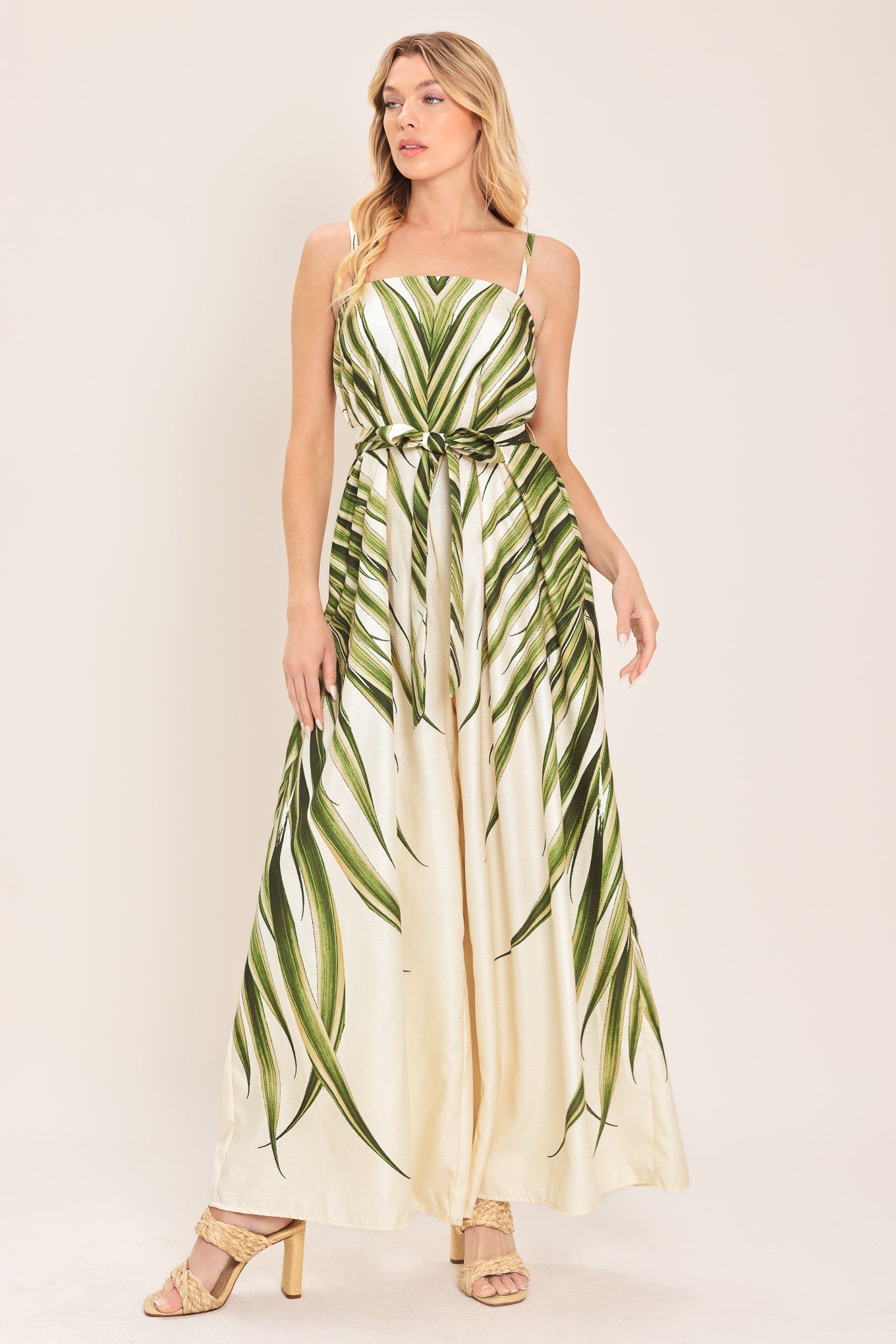 Woman wearing a green and beige wide-leg leaf-patterned jumpsuit featuring straight neckline, straps, and self tie | Flying Tomato