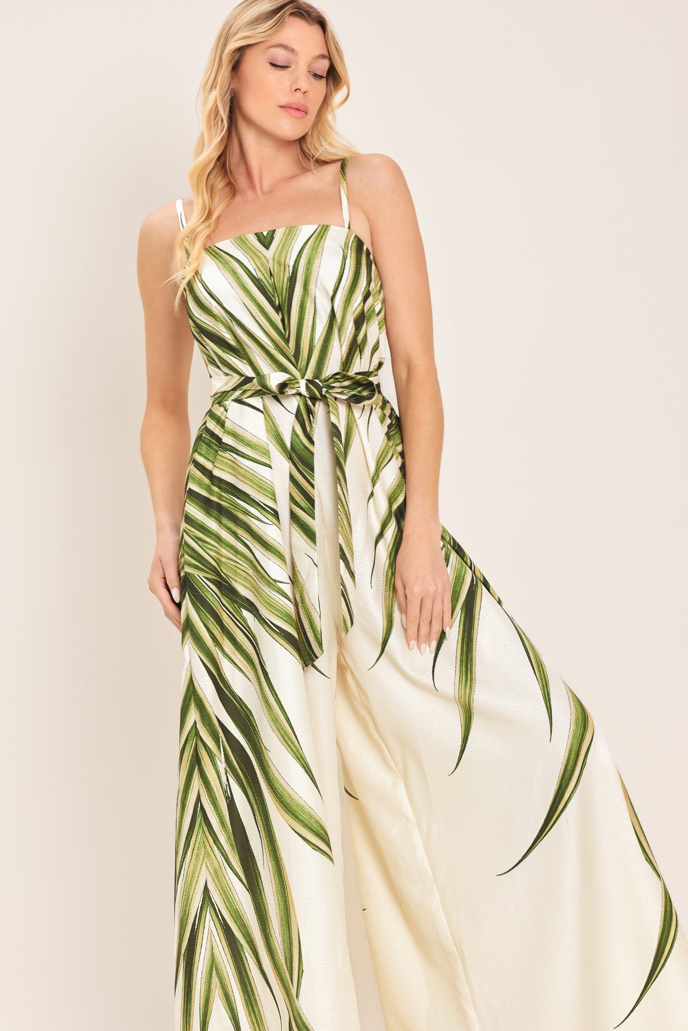 Woman wearing a green and beige wide-leg leaf-patterned jumpsuit featuring straight neckline, straps, and self tie | Flying Tomato