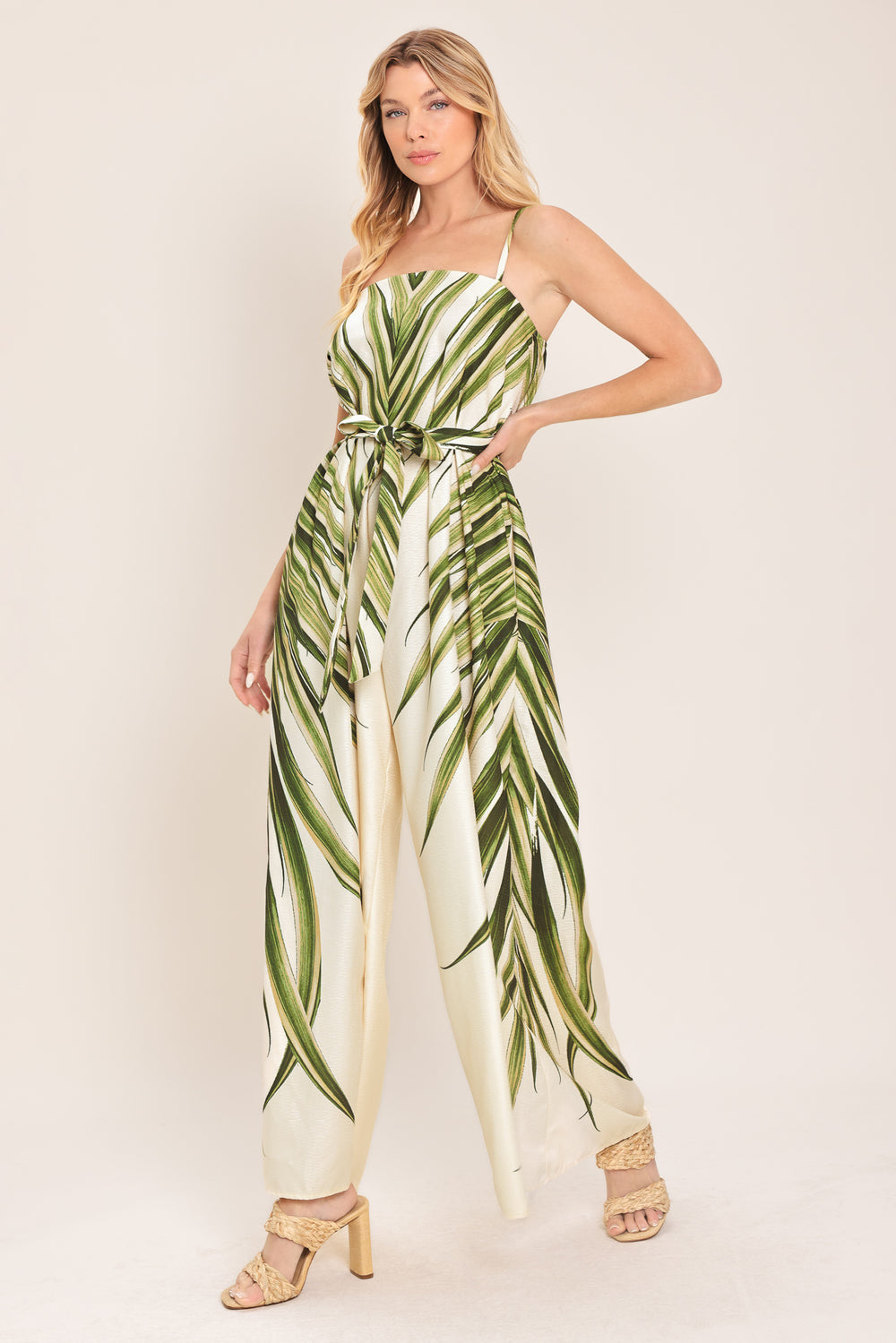 Woman wearing a green and beige wide-leg leaf-patterned jumpsuit featuring straight neckline, straps, and self tie | Flying Tomato
