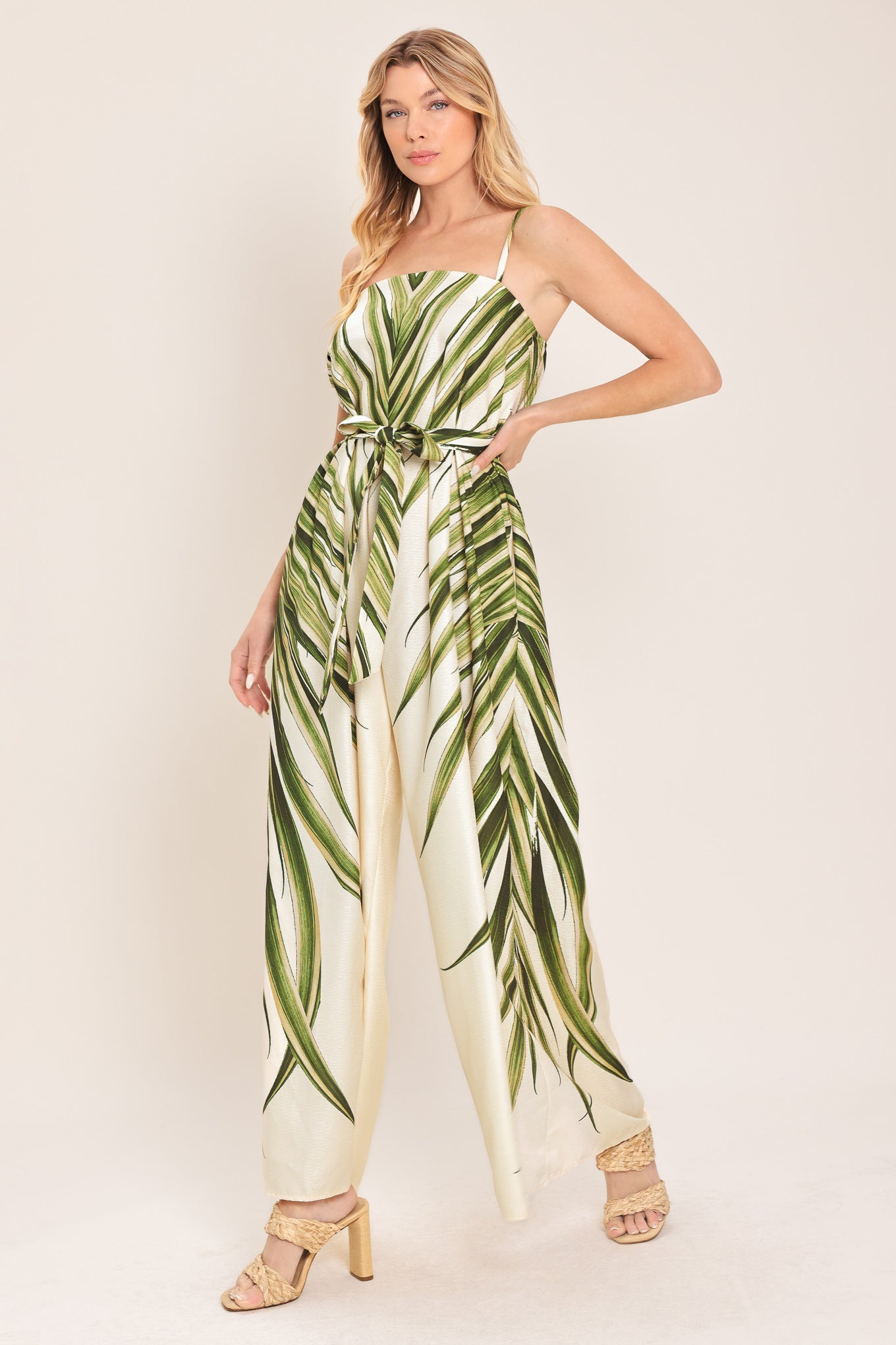 Woman wearing a green and beige wide-leg leaf-patterned jumpsuit featuring straight neckline, straps, and self tie | Flying Tomato