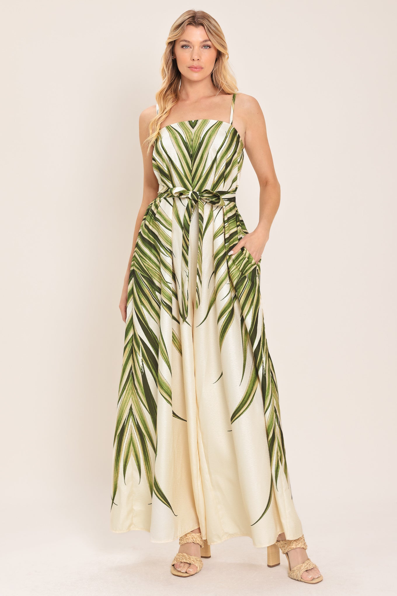 Woman wearing a green and beige wide-leg leaf-patterned jumpsuit featuring straight neckline, straps, and self tie | Flying Tomato