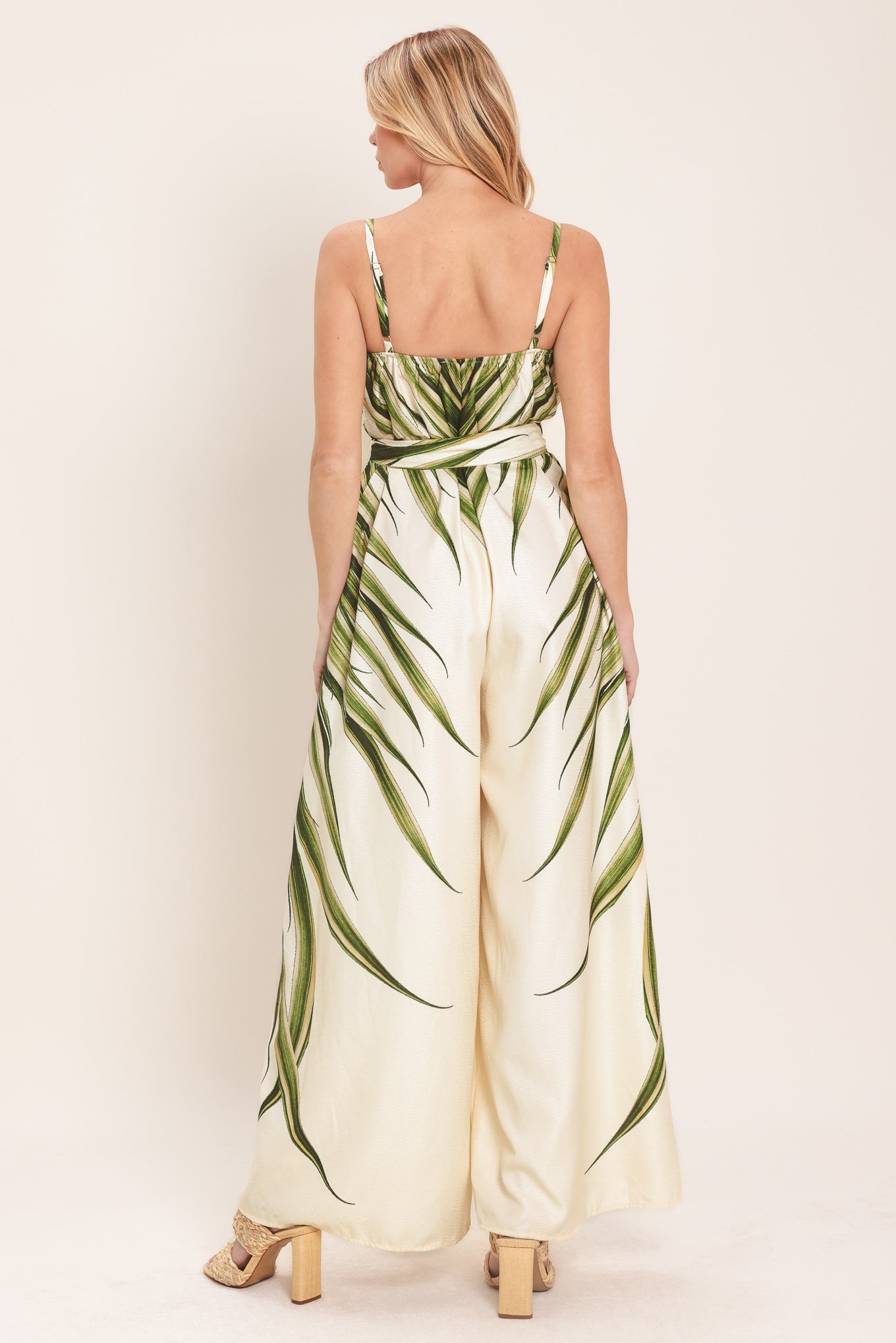 Woman wearing a green and beige wide-leg leaf-patterned jumpsuit featuring straight neckline, straps, and self tie | Flying Tomato