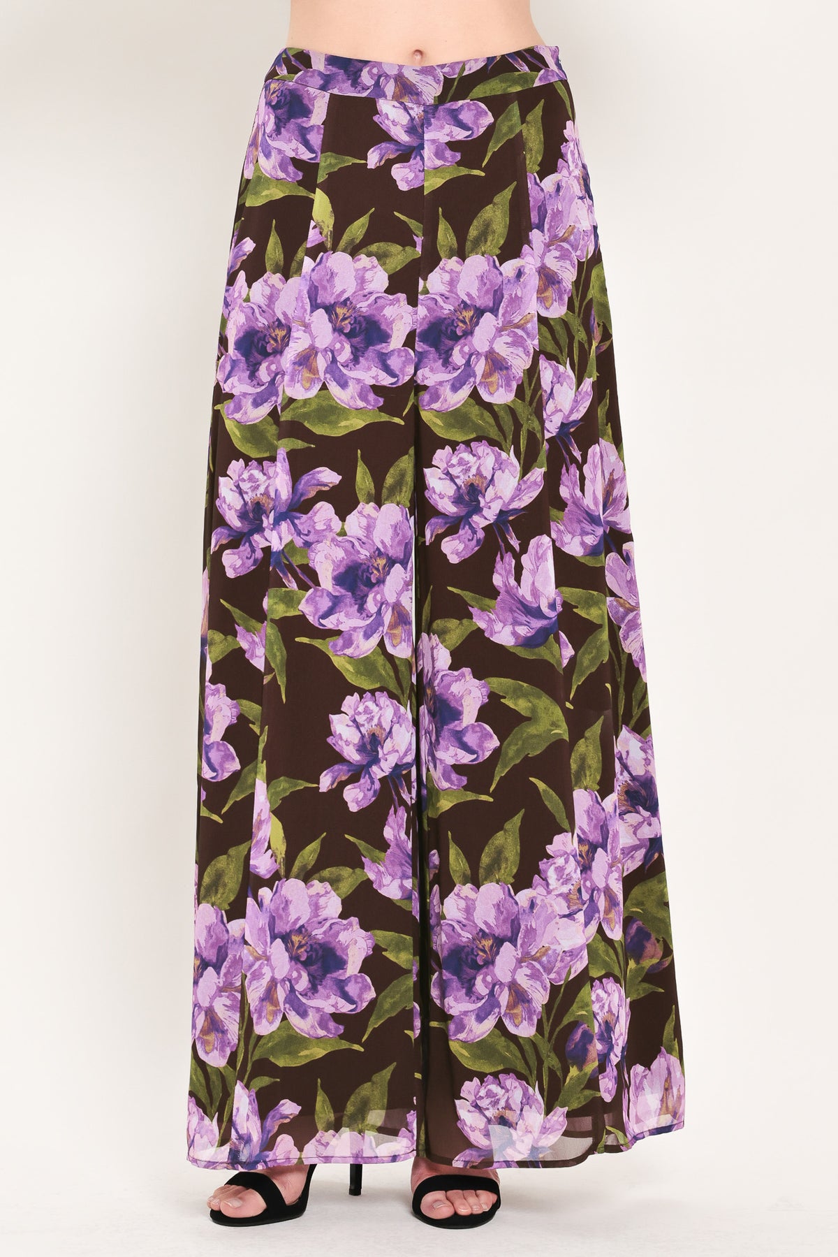 A model is wearing a pair of wide-leg, high-waisted pants featuring a bold purple floral print on a dark brown background | Flying Tomato