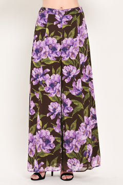 A model is wearing a pair of wide-leg, high-waisted pants featuring a bold purple floral print on a dark brown background | Flying Tomato