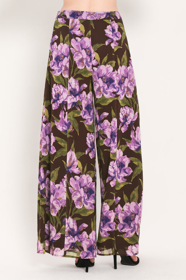A model is wearing a pair of wide-leg, high-waisted pants featuring a bold purple floral print on a dark brown background | Flying Tomato