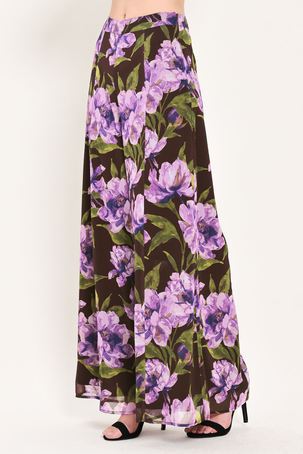 A model is wearing a pair of wide-leg, high-waisted pants featuring a bold purple floral print on a dark brown background | Flying Tomato
