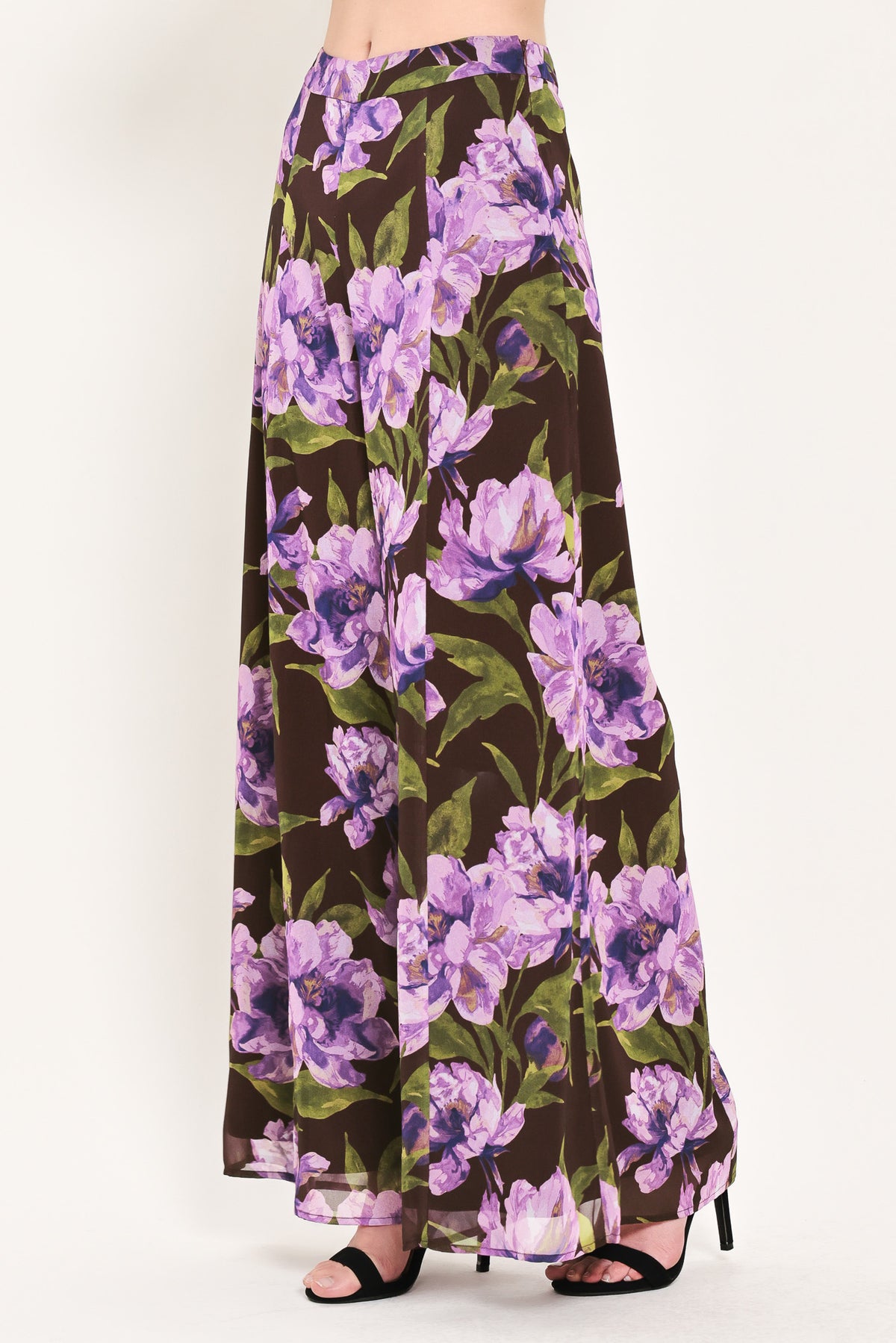 A model is wearing a pair of wide-leg, high-waisted pants featuring a bold purple floral print on a dark brown background | Flying Tomato