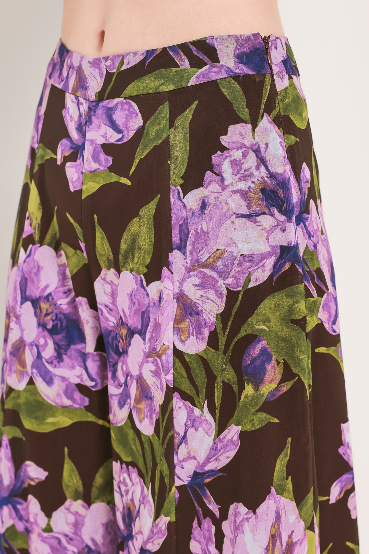 A model is wearing a pair of wide-leg, high-waisted pants featuring a bold purple floral print on a dark brown background | Flying Tomato