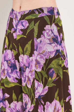 A model is wearing a pair of wide-leg, high-waisted pants featuring a bold purple floral print on a dark brown background | Flying Tomato