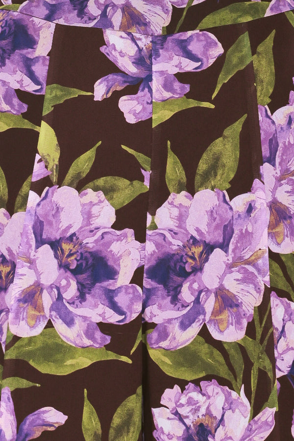 A model is wearing a pair of wide-leg, high-waisted pants featuring a bold purple floral print on a dark brown background | Flying Tomato