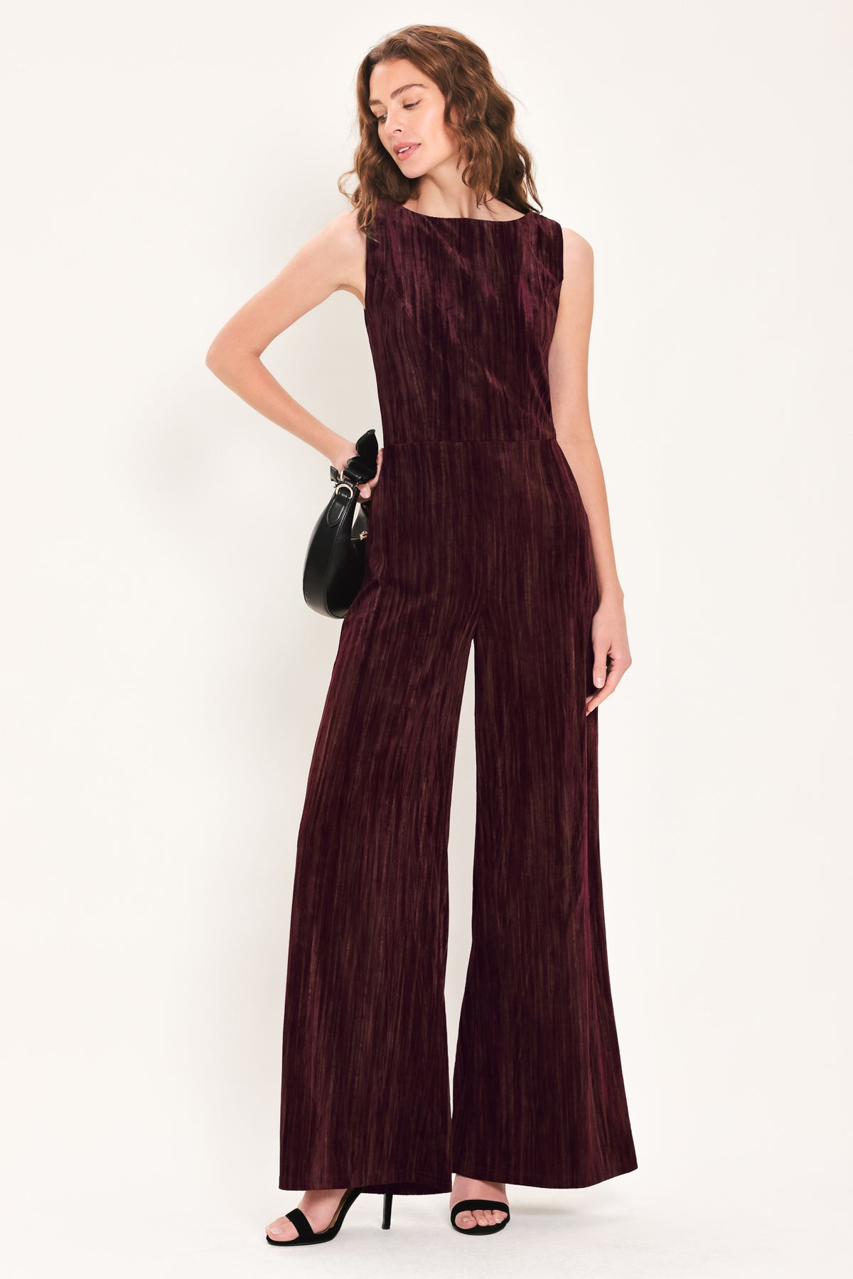 Woman wearing a sleeveless burgundy velvet jumpsuit with wide-leg pants | Flying Tomato