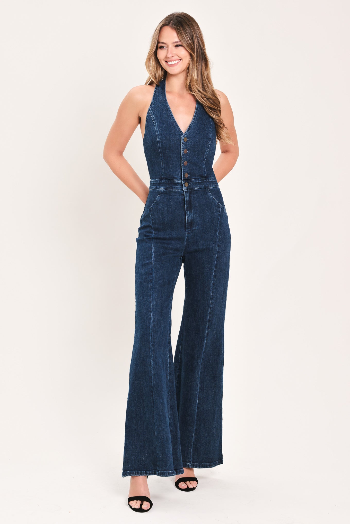 A woman wearing a dark blue denim halter jumpsuit with a button-front bodice and wide flared legs | Flying Tomato 