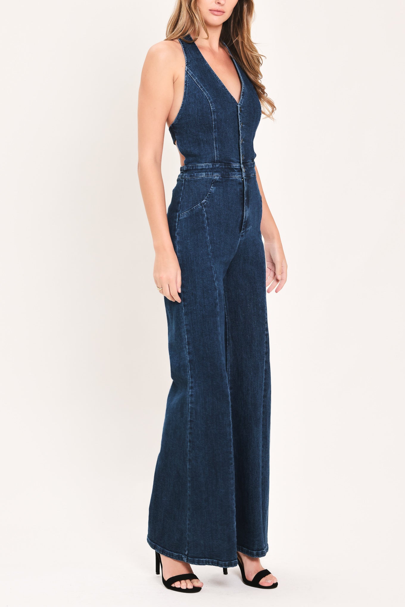 A woman wearing a dark blue denim halter jumpsuit with a button-front bodice and wide flared legs | Flying Tomato 