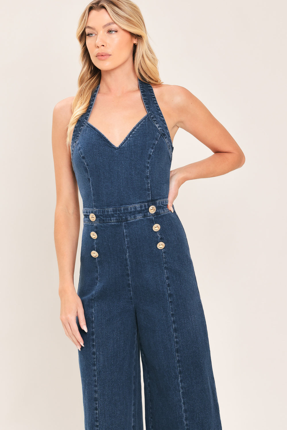 Woman wearing a denim jumpsuit featuring halter neckline, front button detail, wide leg, bare back and zipper closure | Flying Tomato