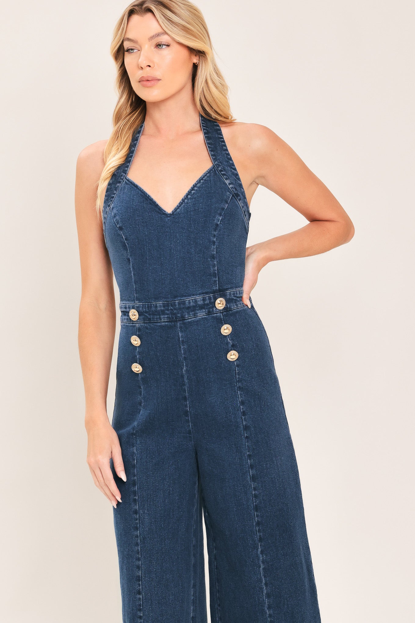 Woman wearing a denim jumpsuit featuring halter neckline, front button detail, wide leg, bare back and zipper closure | Flying Tomato