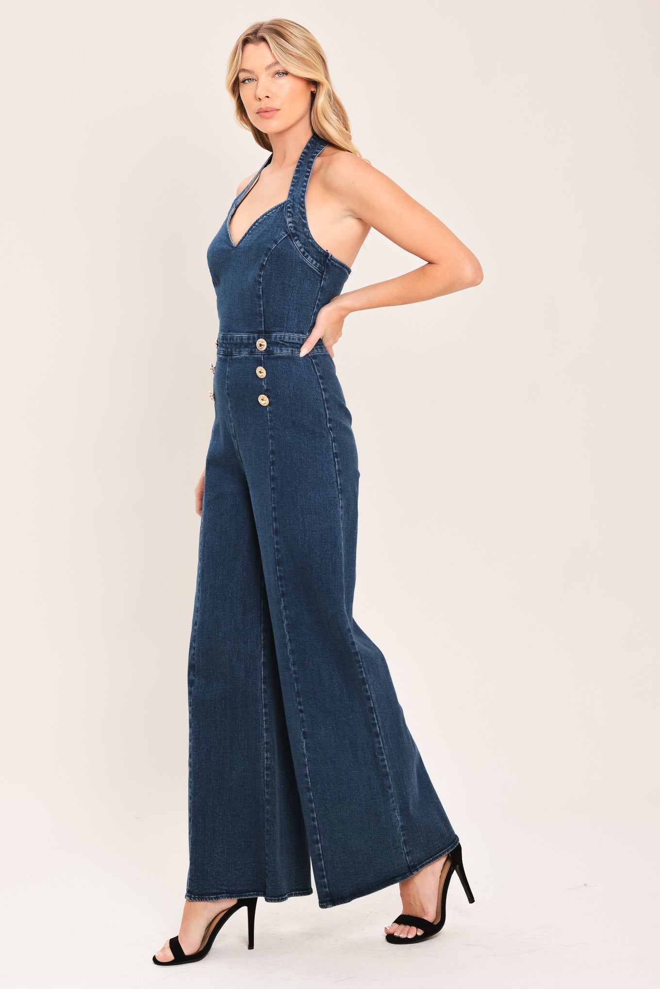 Woman wearing a denim jumpsuit featuring halter neckline, front button detail, wide leg, bare back and zipper closure | Flying Tomato