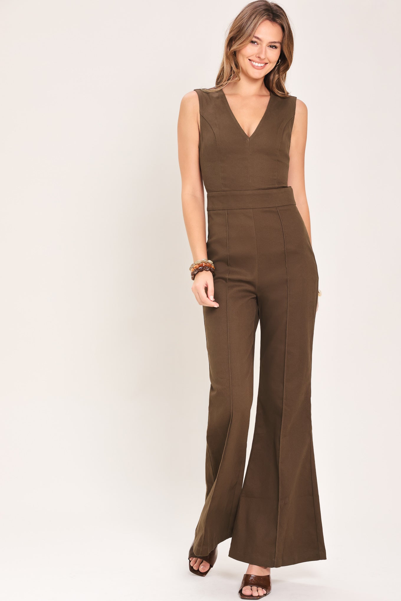 Woman wearing a brown jumpsuit featuring V neckline, sleeveless, flare leg, back cut out and button zipper closure | Flying Tomato