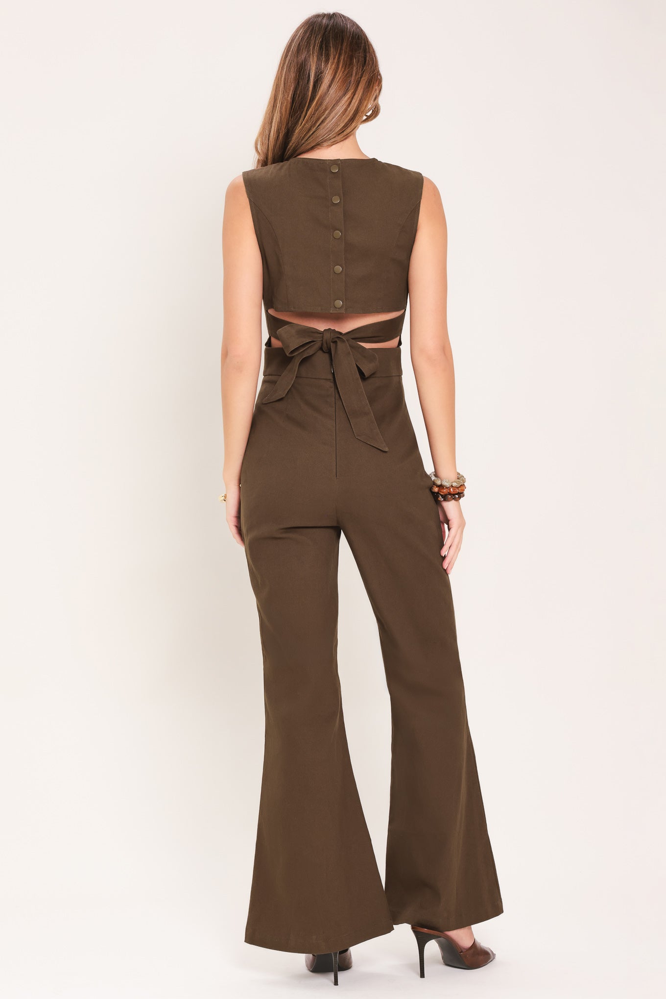 Woman wearing a brown jumpsuit featuring V neckline, sleeveless, flare leg, back cut out and button zipper closure | Flying Tomato