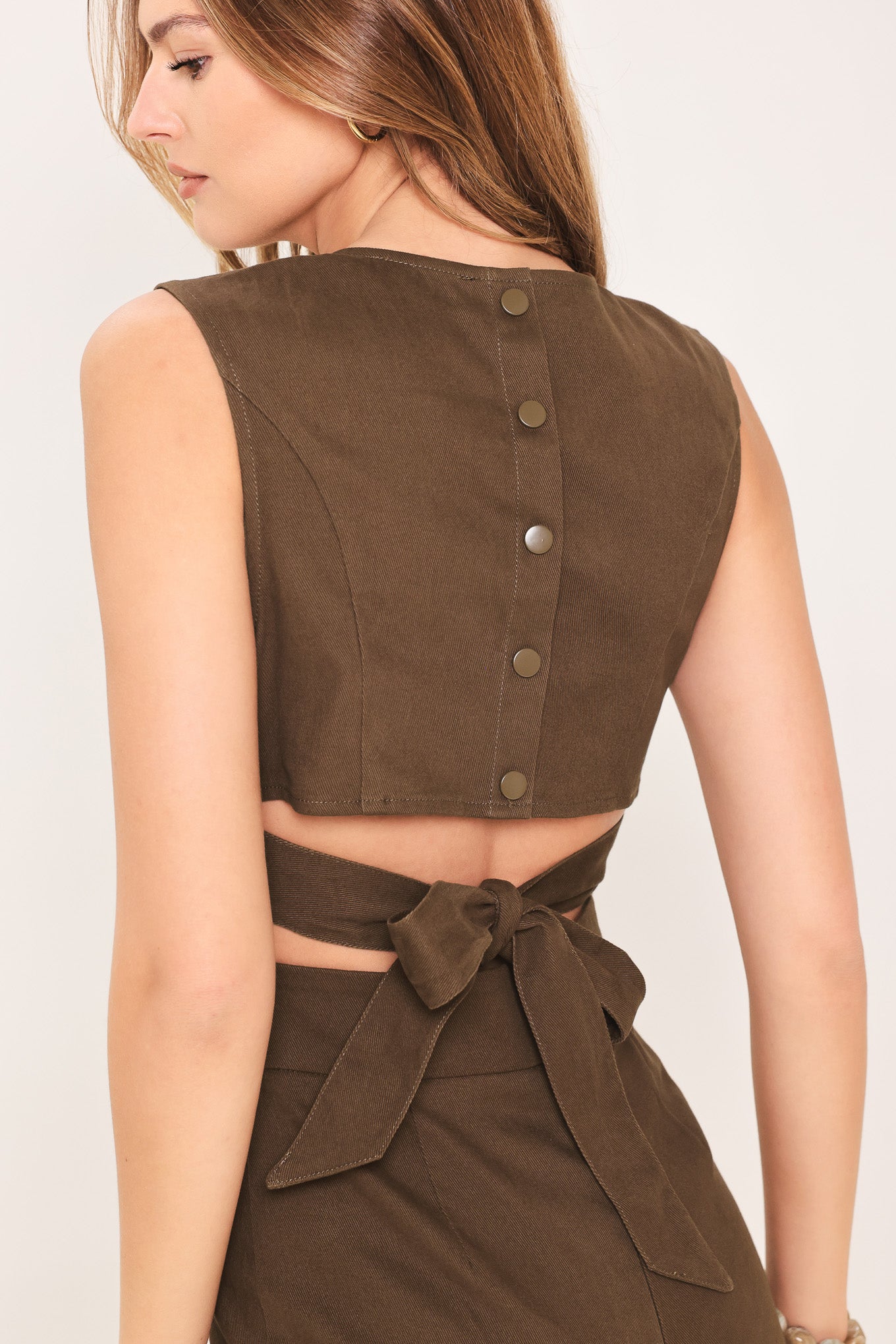 Woman wearing a brown jumpsuit featuring V neckline, sleeveless, flare leg, back cut out and button zipper closure | Flying Tomato
