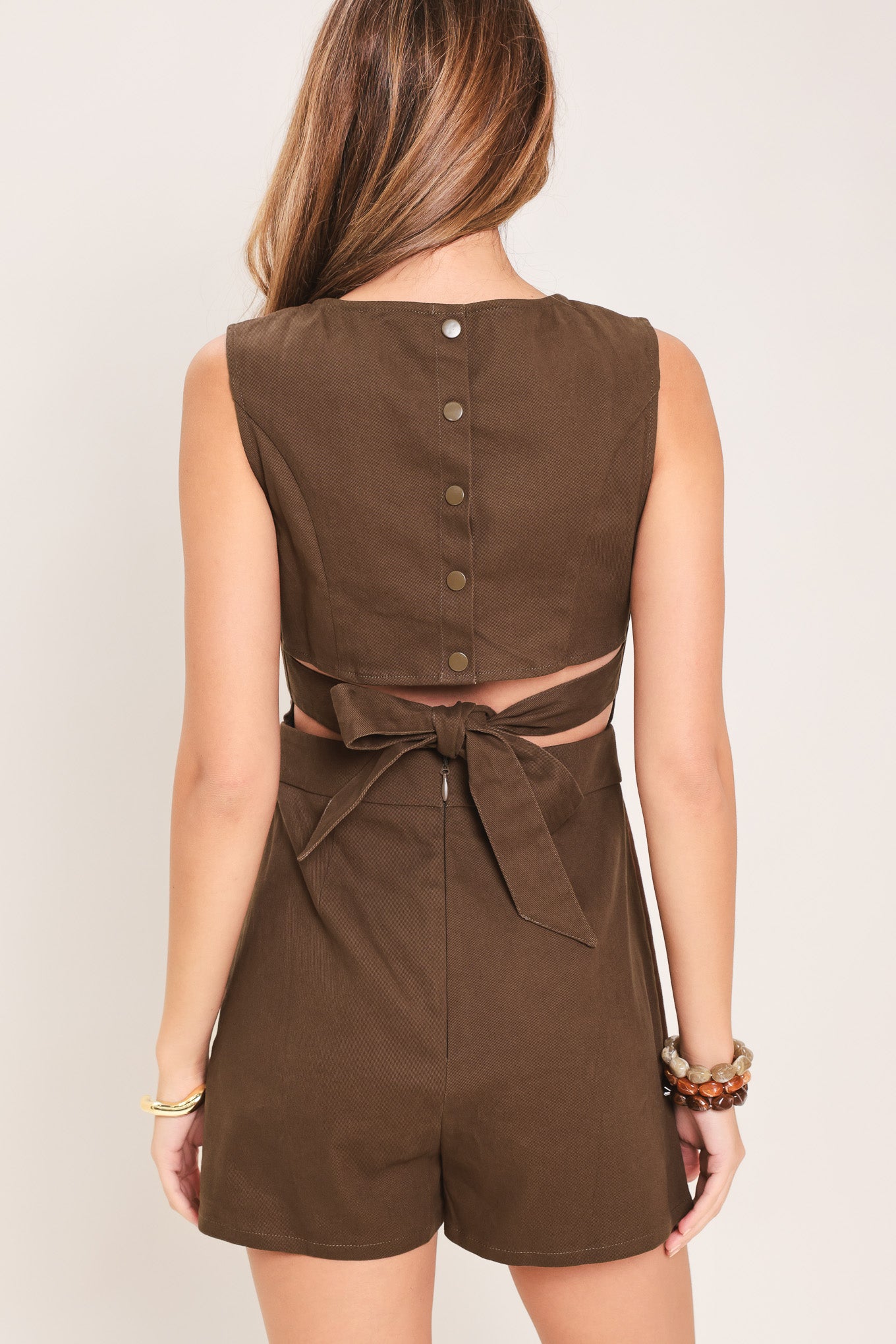 Woman wearing a brown woven skort romper featuring round neckline, sleeveless, back cut out with tie and button zipper closure | Flying Tomato