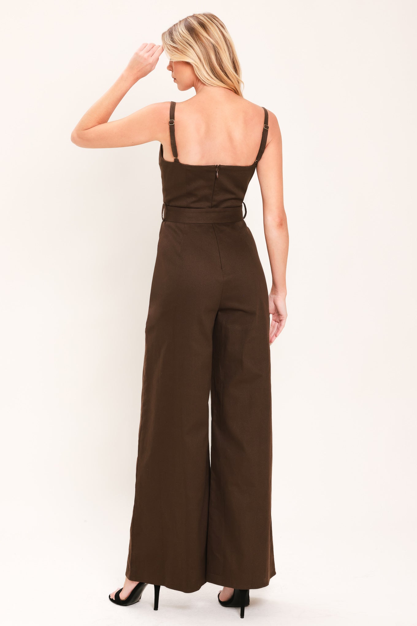 Woman wearing a brown solid woven jumpsuit featuring sweetheart neckline, straps, self belt, wide leg and back zipper closure | Flying Tomato