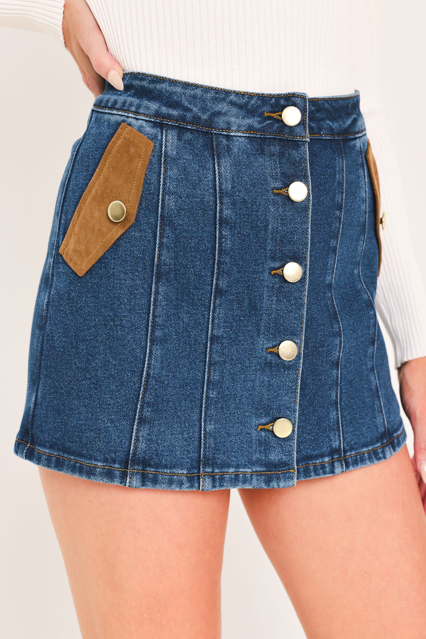 A blue denim mini skort with a button-front closure and brown suede-like side pockets, shown on a model | Flying Tomato