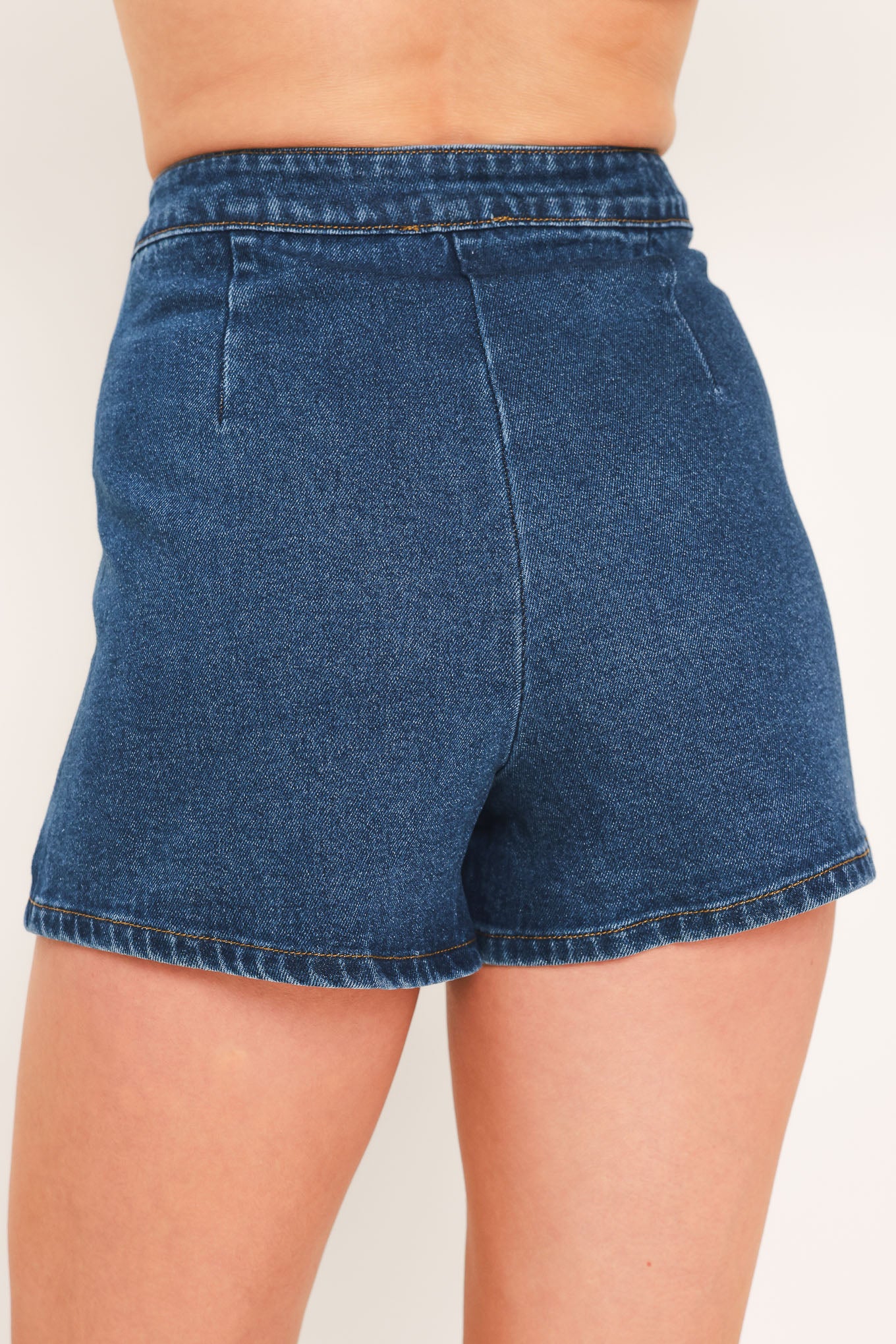 A blue denim mini skort with a button-front closure and brown suede-like side pockets, shown on a model | Flying Tomato