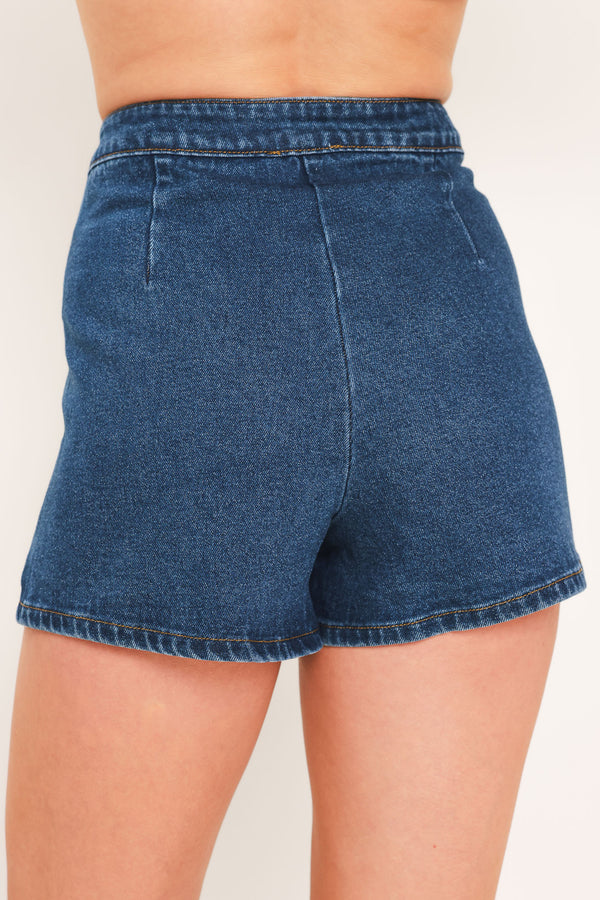A blue denim mini skort with a button-front closure and brown suede-like side pockets, shown on a model | Flying Tomato
