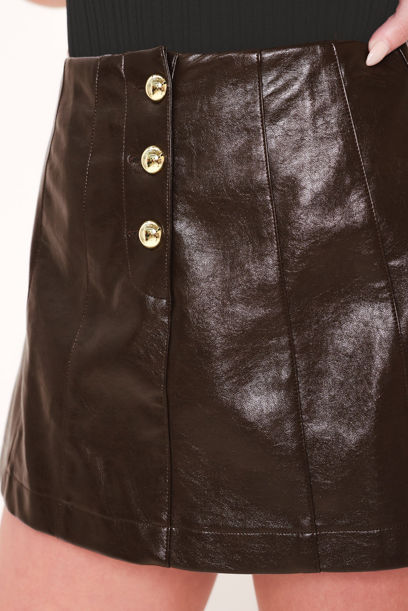 Woman wearing a dark brown faux leather skort with gold buttons on the front | Flying Tomato