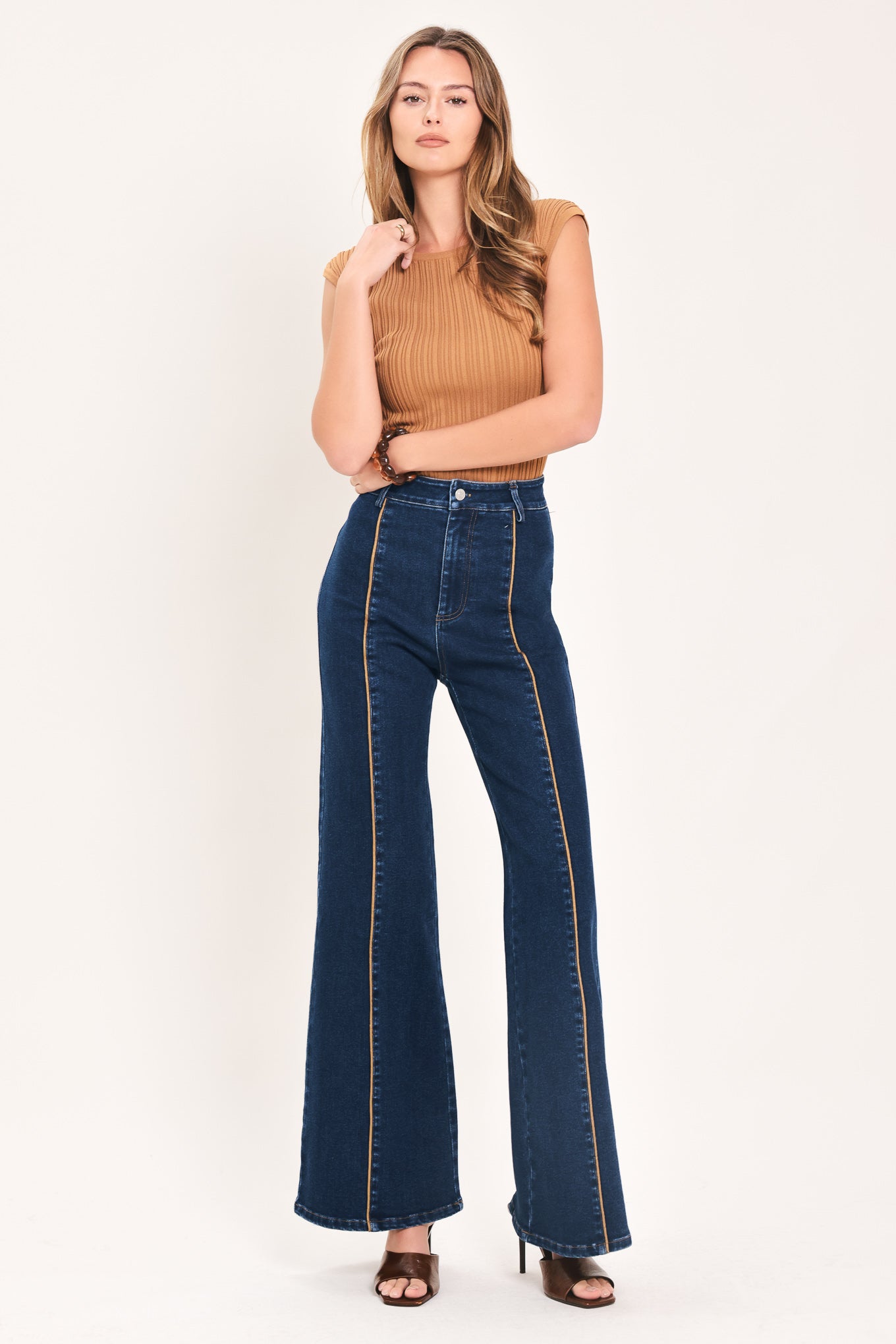 A model wearing dark blue high-waisted flare jeans with distinctive gold-colored contrast stitching running down the center of the legs | Flying Tomato