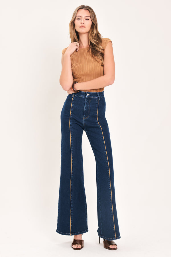 A model wearing dark blue high-waisted flare jeans with distinctive gold-colored contrast stitching running down the center of the legs | Flying Tomato