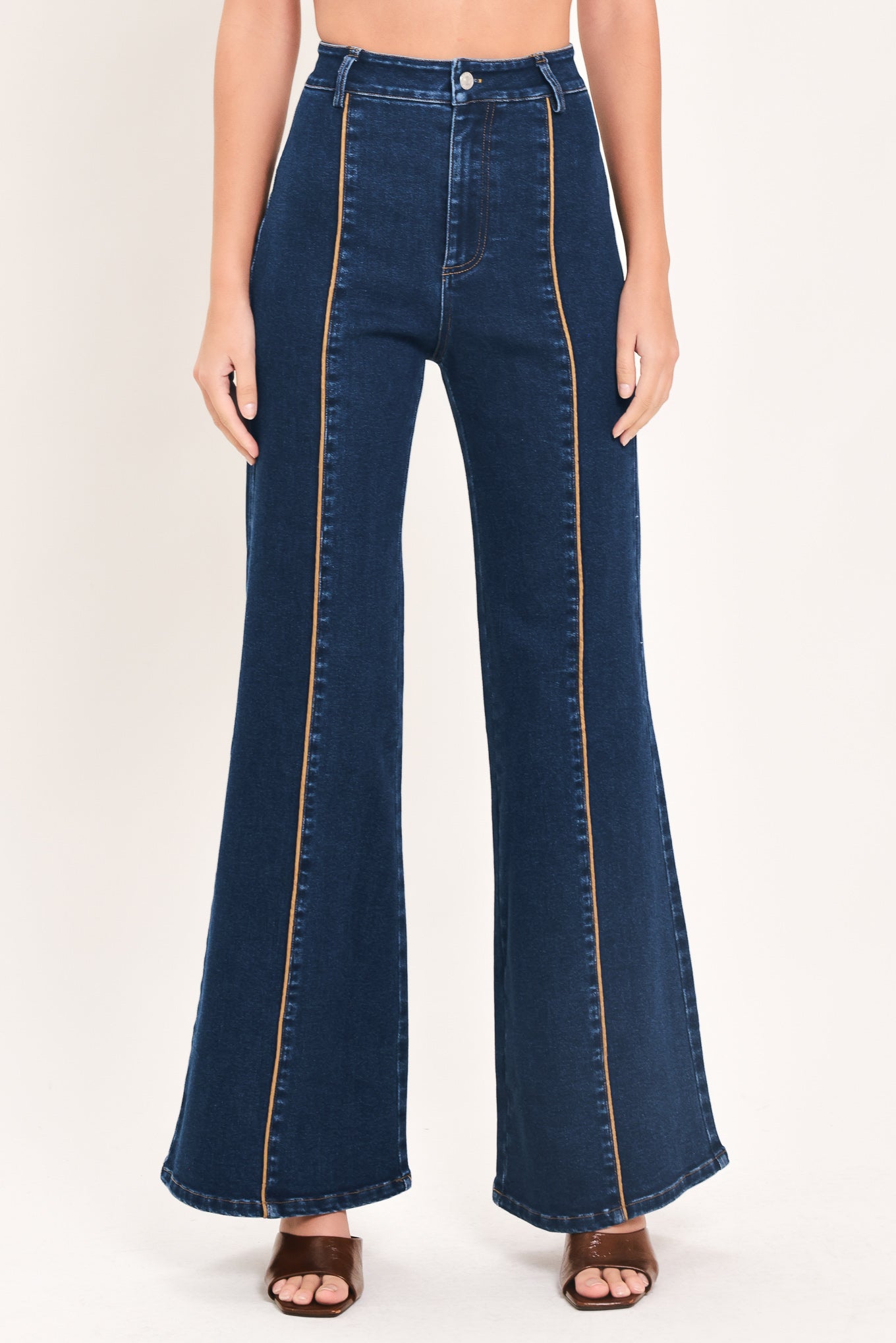 A model wearing dark blue high-waisted flare jeans with distinctive gold-colored contrast stitching running down the center of the legs | Flying Tomato