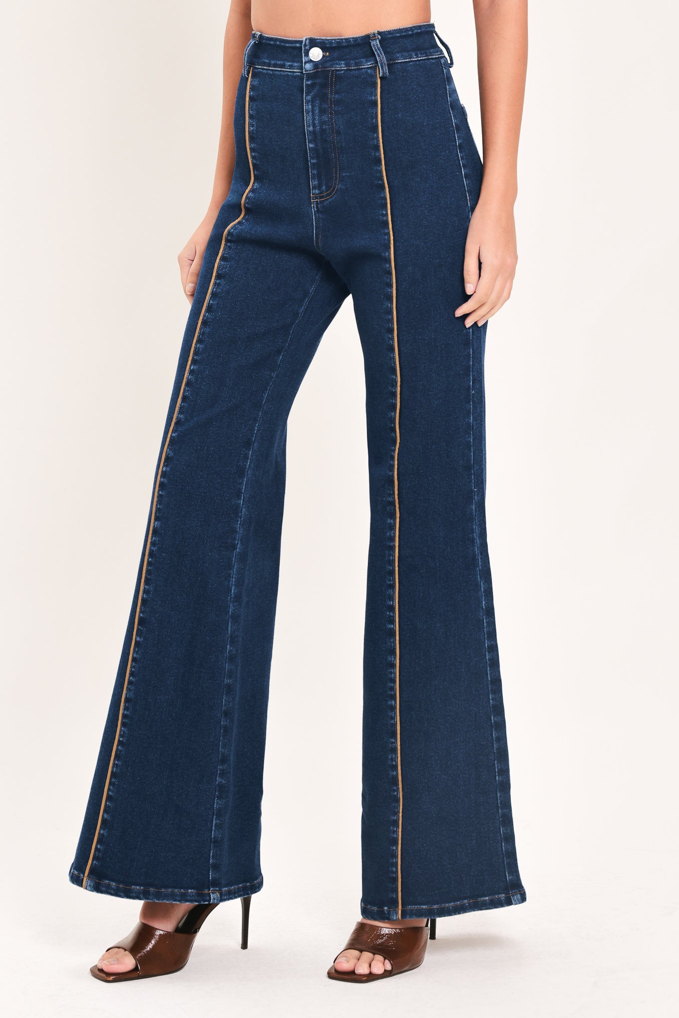A model wearing dark blue high-waisted flare jeans with distinctive gold-colored contrast stitching running down the center of the legs | Flying Tomato