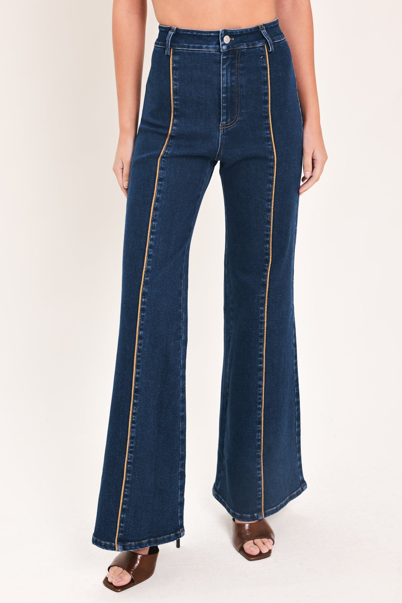 A model wearing dark blue high-waisted flare jeans with distinctive gold-colored contrast stitching running down the center of the legs | Flying Tomato