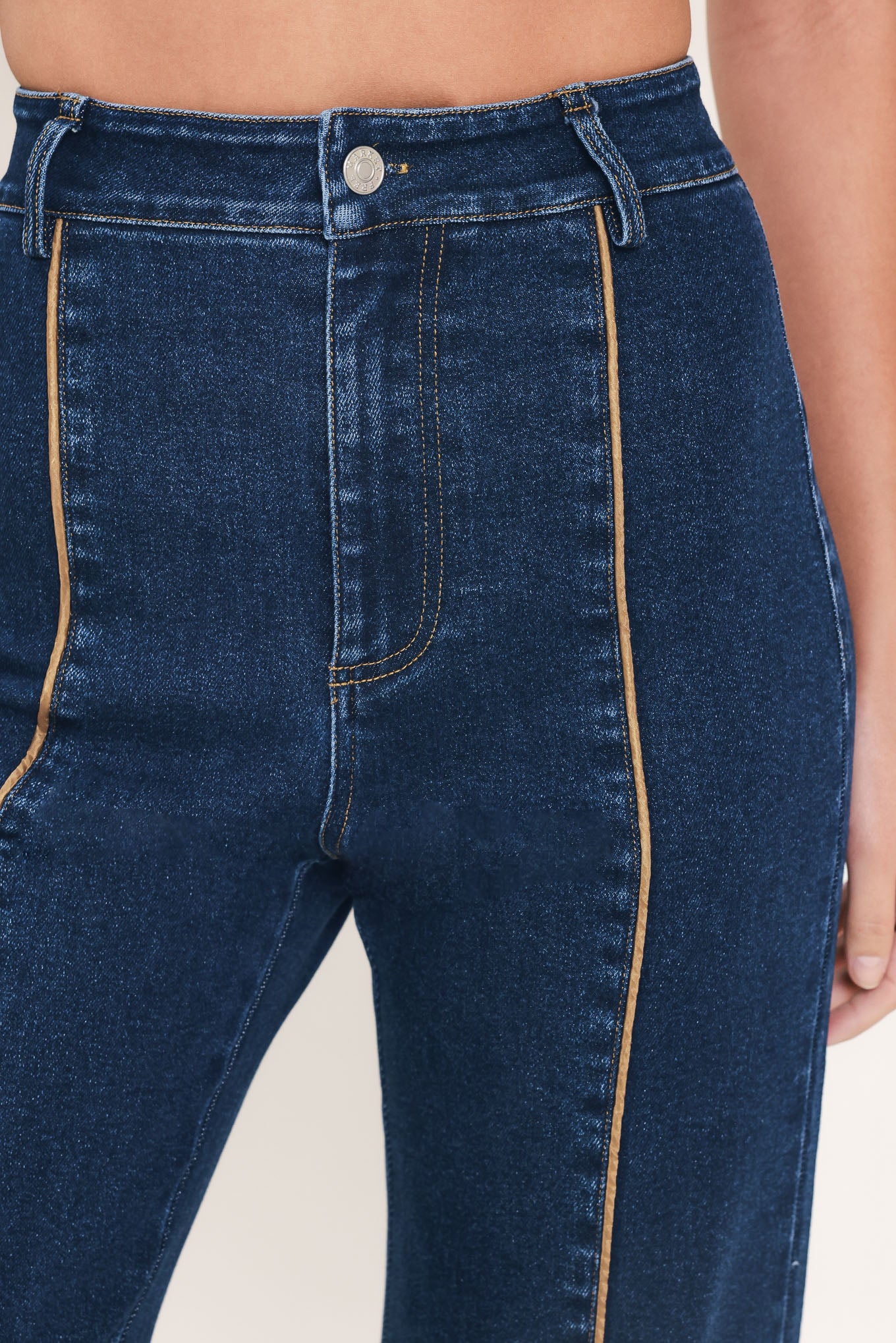 A model wearing dark blue high-waisted flare jeans with distinctive gold-colored contrast stitching running down the center of the legs | Flying Tomato