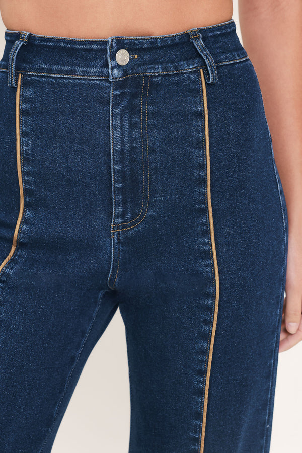 A model wearing dark blue high-waisted flare jeans with distinctive gold-colored contrast stitching running down the center of the legs | Flying Tomato