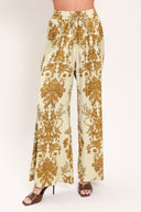 A woman wearing high-waisted, wide-leg pants with a beige base and an ornate gold damask pattern | Flying Tomato