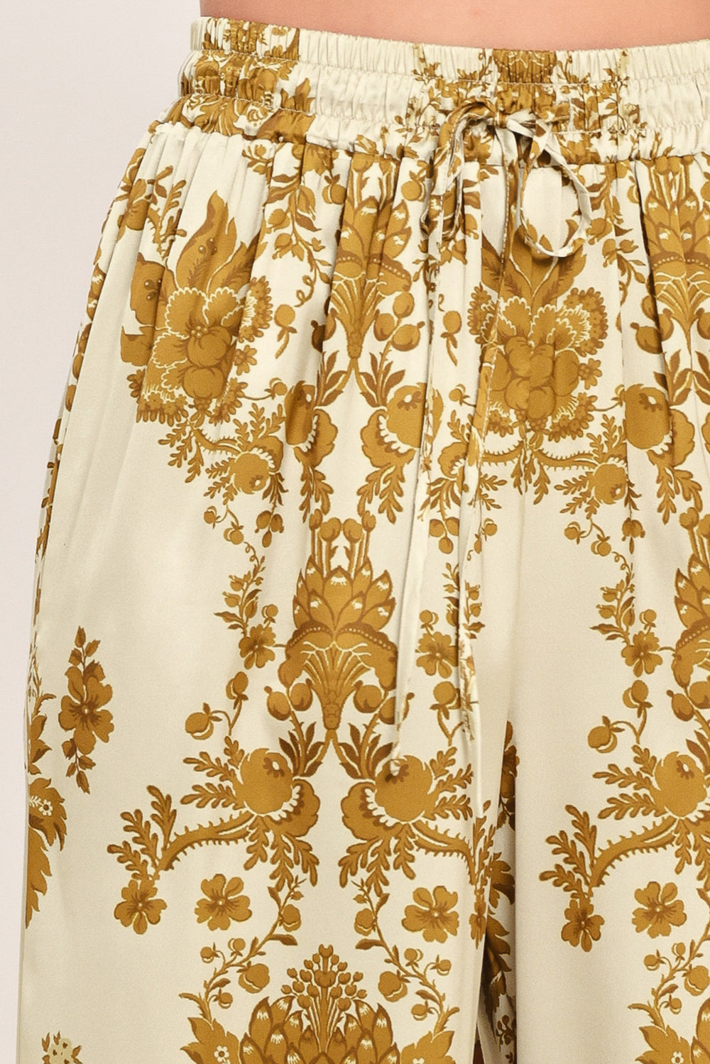 A woman wearing high-waisted, wide-leg pants with a beige base and an ornate gold damask pattern | Flying Tomato