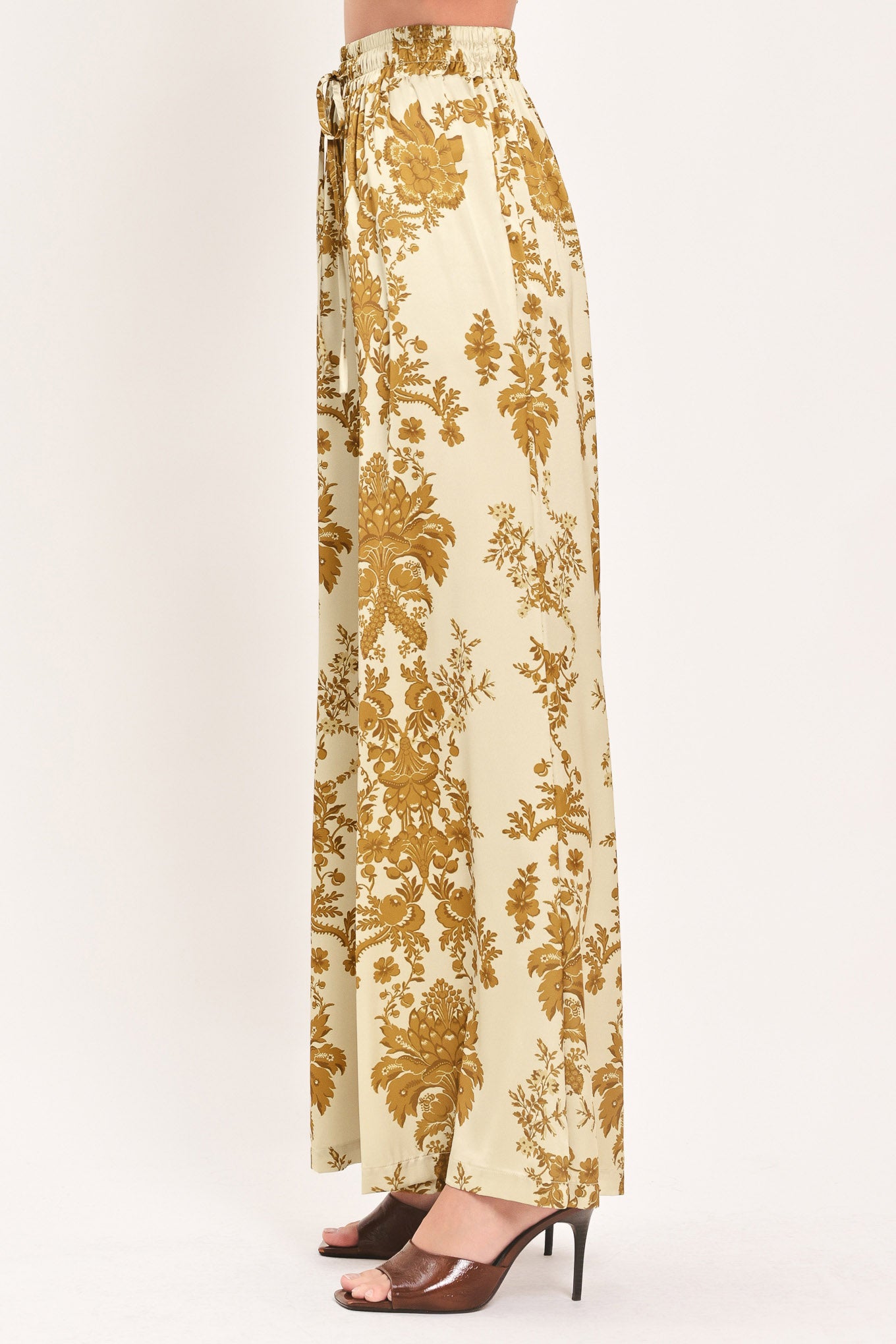 A woman wearing high-waisted, wide-leg pants with a beige base and an ornate gold damask pattern | Flying Tomato