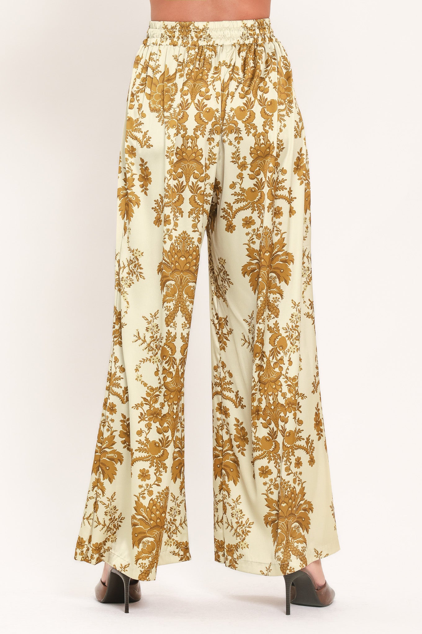 A woman wearing high-waisted, wide-leg pants with a beige base and an ornate gold damask pattern | Flying Tomato