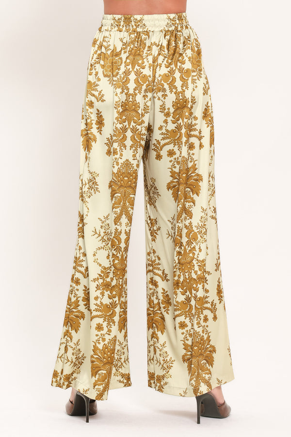 A woman wearing high-waisted, wide-leg pants with a beige base and an ornate gold damask pattern | Flying Tomato