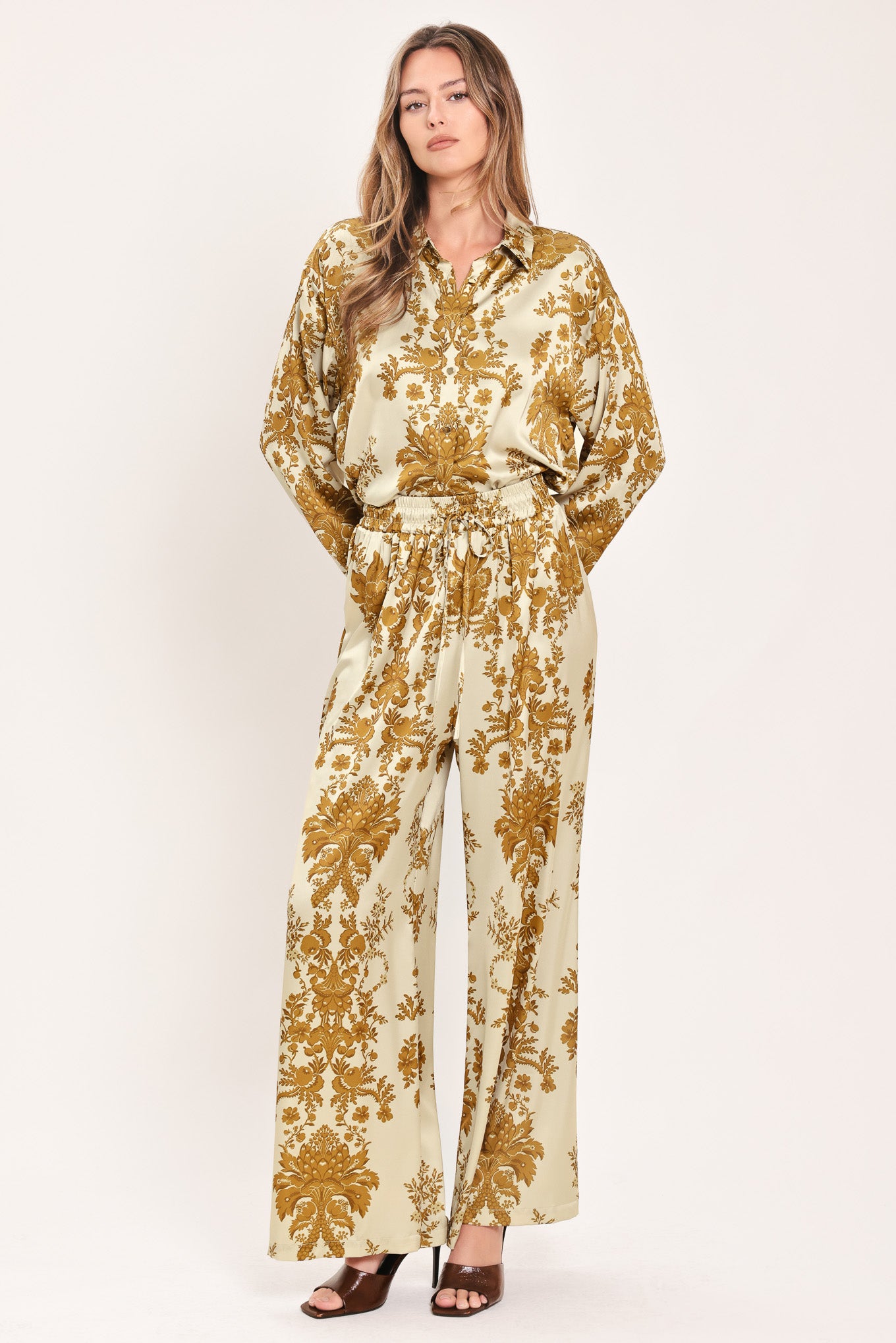 A woman wearing high-waisted, wide-leg pants with a beige base and an ornate gold damask pattern | Flying Tomato