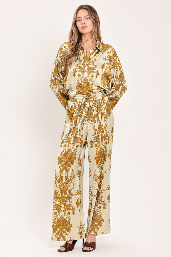 A woman wearing high-waisted, wide-leg pants with a beige base and an ornate gold damask pattern | Flying Tomato