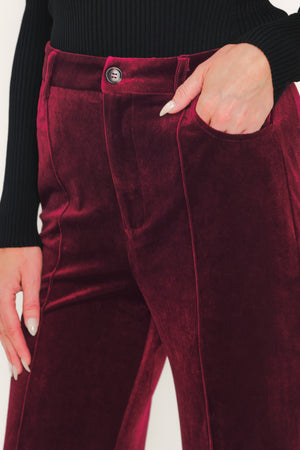 A pair of high-waisted, wide-leg velvet pants in a deep burgundy red, shown on a model | Flying Tomato
