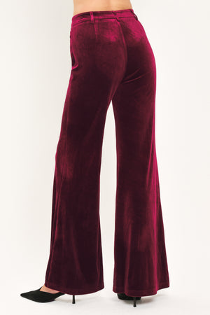 A pair of high-waisted, wide-leg velvet pants in a deep burgundy red, shown on a model | Flying Tomato